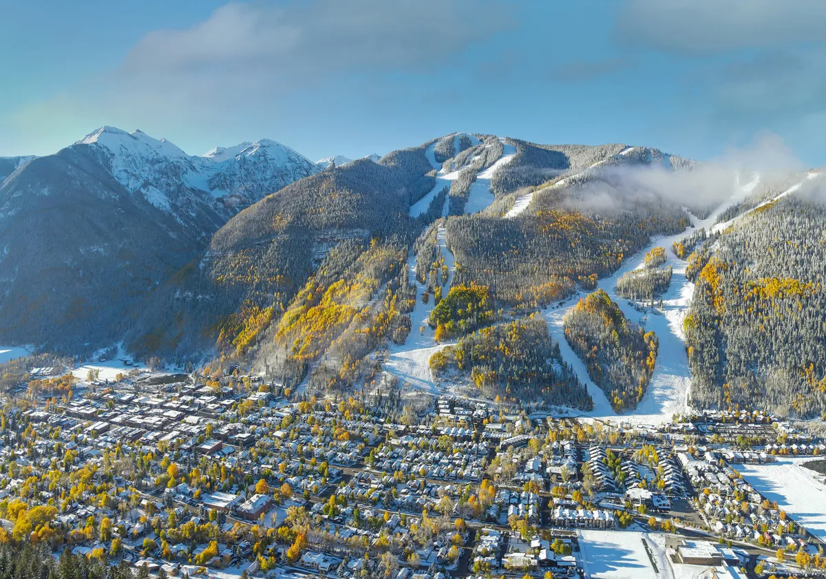 A sweeping view over Telluride reveals snow-capped peaks, ski slopes, colorful trees, and the charming town nestled below. The scenery is both inviting and adventurous, capturing the essence of the ski and outdoor experience.