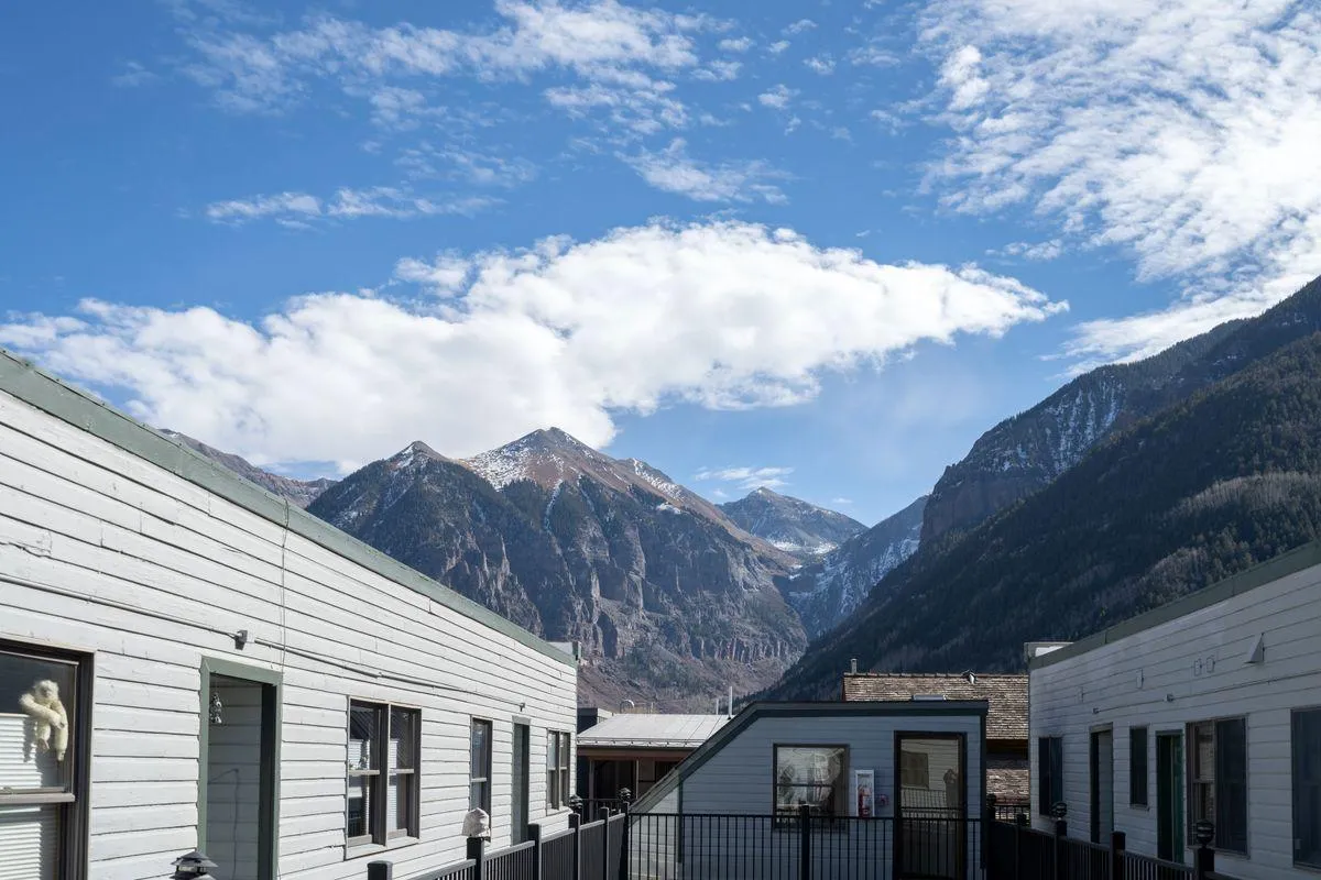 A tranquil view over Telluride’s rooftops, with a majestic mountain range and expansive sky, creates a serene backdrop. The setting sun or dusk light hints at the quiet beauty that can be found during a sunset stroll along the river.