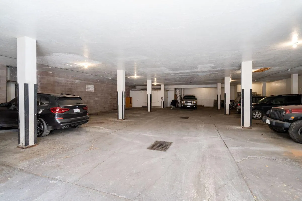 This image shows the interior of the garage with several vehicles parked among support columns and illuminated by fixtures above. The space appears organized and practical, emphasizing the security and accessibility of parking within the complex.